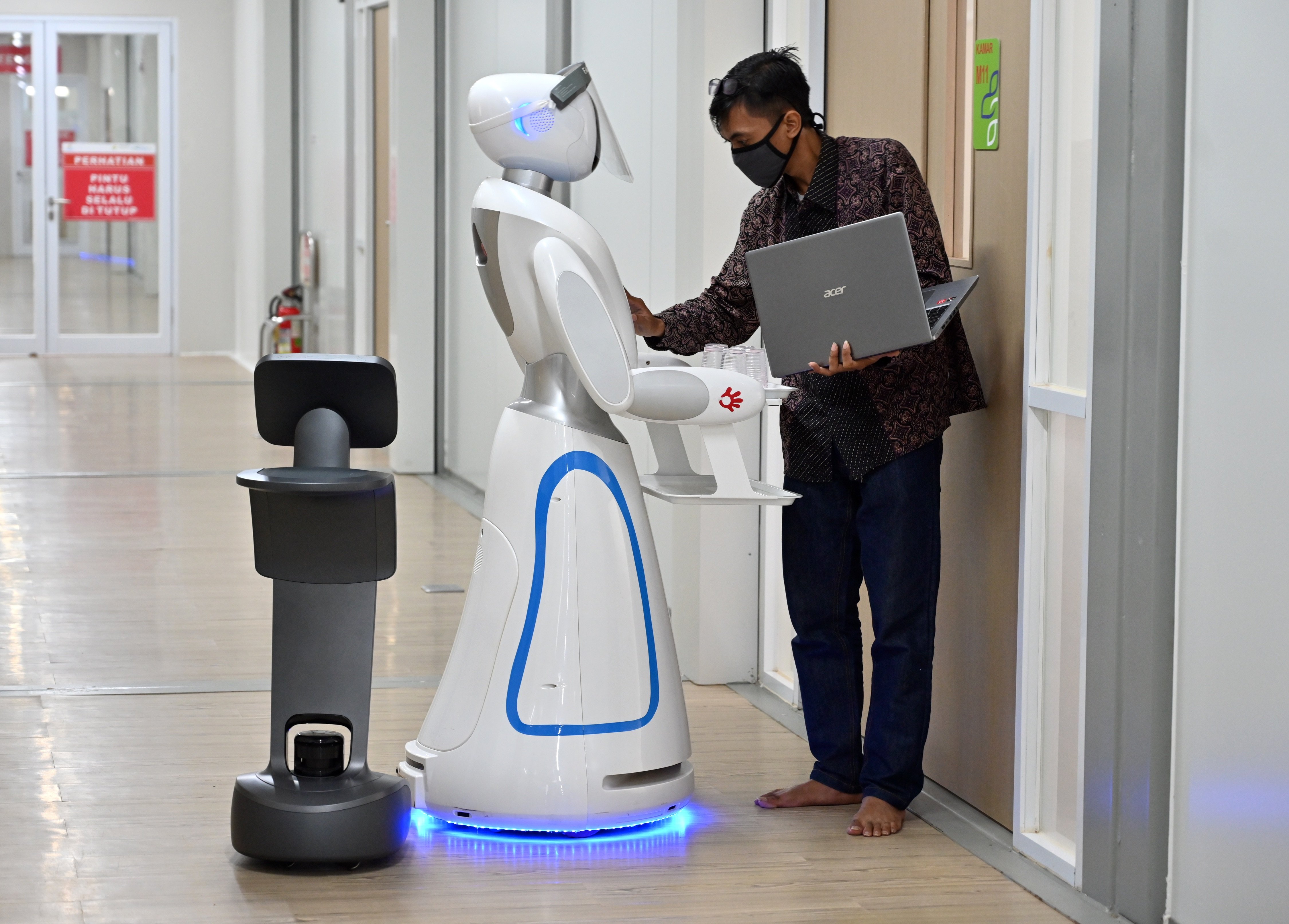 An Indonesian technician (R) examining robots known as Amy (C) and Temi (L) (black) during a simulation on assisting medical teams in handling COVID-19. Source: AFP